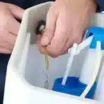 Person adjusts the flush lever and chain inside an open toilet tank