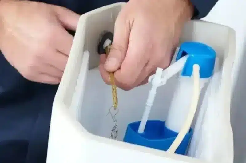 Person adjusts the flush lever and chain inside an open toilet tank